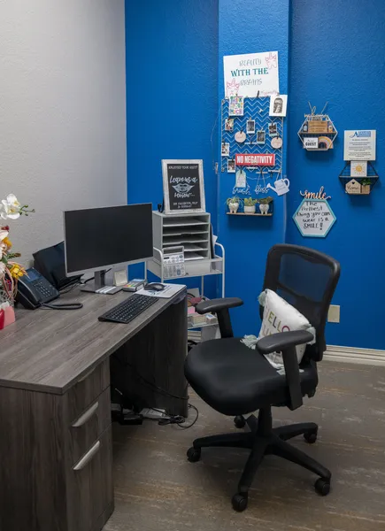 A desk with a computer and a chair in a room with a blue wall.
